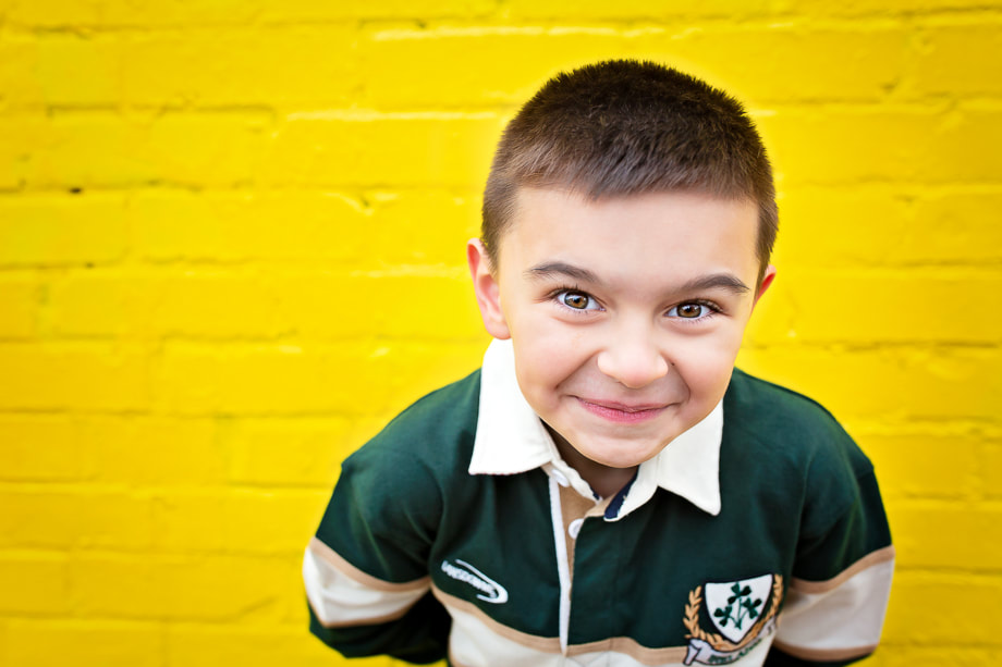 Take a moment to appreciate the pure joy and wonder captured in this photograph of a young child, photographed against a bright yellow wall in historic Old Town Alexandria. The child's beaming smile and sparkling eyes are a testament to the skill and sensitivity of photographer Tamieka Smith, who has expertly captured the child's essence in this stunning portrait. The yellow wall adds an extra layer of vibrancy and energy to the photograph, creating a sense of warmth and happiness that is palpable. This photograph is a true work of art, a celebration of childhood, and a reminder of the beauty and wonder that can be found in the simple moments of life. It's a treasure that the family will cherish for years to come.