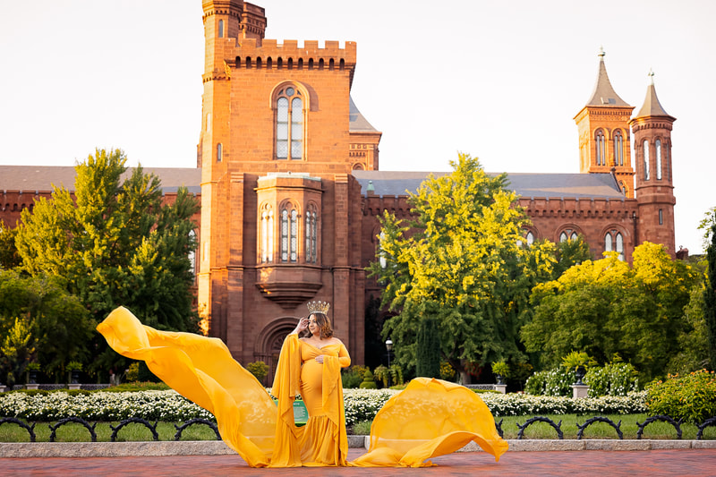 An expectant mother being photographed by Northern Virginia maternity photographer Tamieka Smith in Washington D.C. The mother is standing in front of the Smithsonian Castle in Washington D.C.,  wearing a long yellow flowing dress that shows off her baby bump and gently cradling her belly with a serene expression on her face.