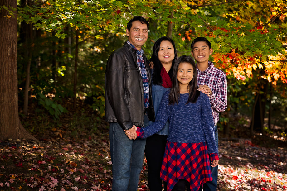 A family portrait session captured in a local Fairfax, Virginia neighborhood by a skilled Northern Virginia family photographer. The image shows four family standing in front of a beautifully manicured lawn and a house in the background. The family members are dressed in coordinating outfits that complement the setting, and the image is framed to include the entire family from head to toe. This local neighborhood in Northern Virginia is an excellent option for an outdoor family photoshoot location near me, as it provides a comfortable and familiar setting that captures the essence of the family's daily life.