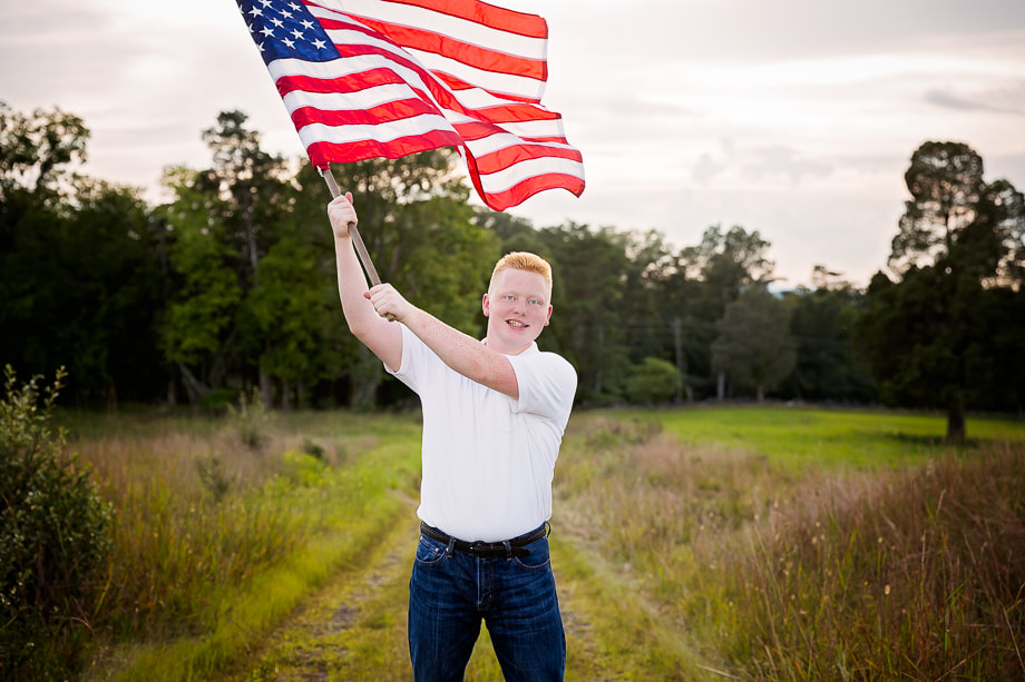 Marvel at this powerful and patriotic photograph of a high school senior waving the American flag at the historic Manassas Battlefield park, captured with expert skill and artistry by Northern Virginia Family photographer Tamieka Smith. The senior's proud stance and confident expression convey a sense of courage and determination, while the flag represents the strength and resilience of our nation. Tamieka has skillfully framed the shot to capture the essence of the moment, with the serene landscape and historic monuments in the background adding an extra layer of depth and meaning. This photograph is a powerful reminder of the sacrifice and dedication of those who have served our country, and a celebration of the potential and promise of the next generation. It's a treasure that the senior and their family will cherish for years to come, a symbol of pride, honor, and hope.