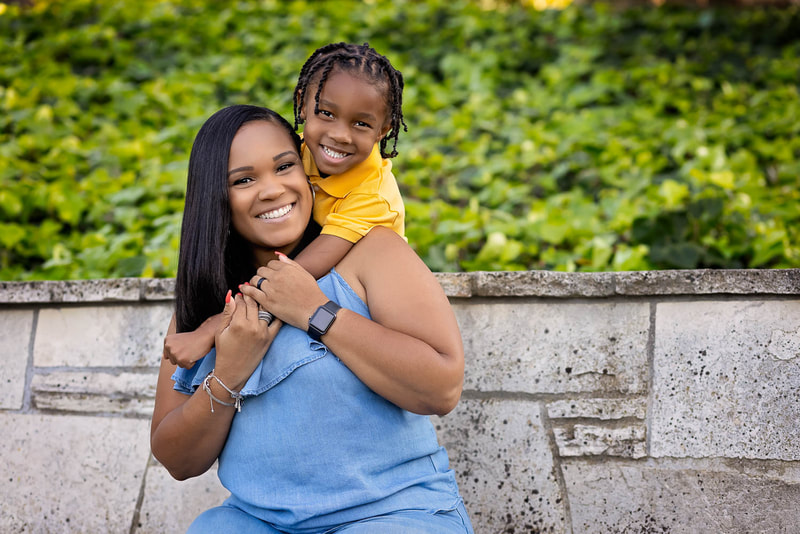A mother and her young son posing together for a family portrait session with South Bay photographer Tamieka Smith. They are sitting at the Malaga Cove Libary with the sun shining down on them, both wearing bright, happy expressions.